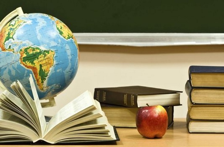 books on a teacher's desk with globe of the Earth and an apple